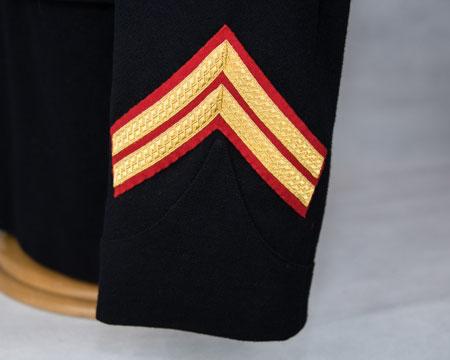 Lyre badge immediately above inside angle of upper chevron Bd Cpl rank badge: Chevrons (gold on red) surmounted by an embroidered lyre (gold on dark blue) Upper right arm - centrally, point of lowest