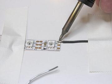 Line up the first wire with the strip, either with a helping hands tool, or just tape both down to a working surface, then solder the connection between them.
