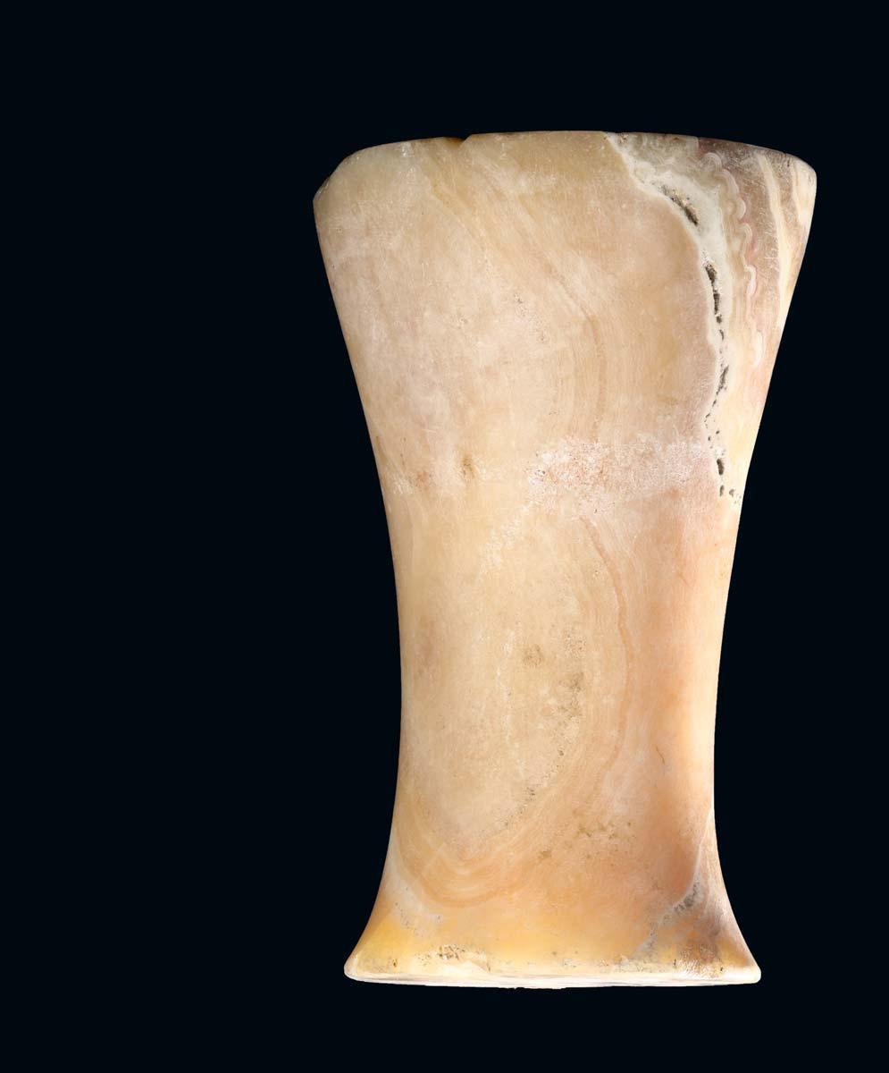 40 A BACTRIAN BANDED ALABASTER RITUAL OBJECT Circa late 3rd early 2nd Millennium B.C. Of typical waisted cylindrical shape, with a groove on each flat face, the natural banding of the stone forming abstract patterns in shades of pink, yellow and white, 22cm high.