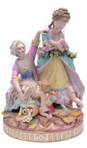 A Meissen Marcolini porcelain figure group modelled as two ladies, one bound by a floral garland with a mischievous cupid in her under skirts with a second cupid kneeling before her seated companion