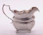 A George III Irish cream jug of barge shaped outline, monogrammed, with gadrooned border and foliate engraved cushion girdle, raised on ball feet,