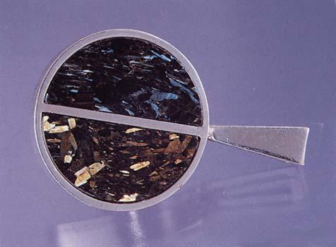 Figure 20. This pendant (about 2 cm in diameter) contains two half-disks of iridescent orthoamphibole ( Nuummite ). Courtesy of Greenland Resources A/S; photo by Maha Tannous.