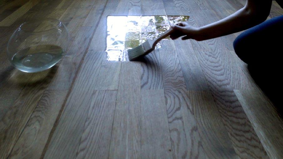 A hand with a paintbrush starts to coat the floor with water.