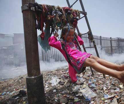 Fig. 1.5 - Sana, a 5-year-old girl, plays on a cloth sling hanging from a signaling pole as smoke from a garbage dump rises next to a railway track in Mumbai, India, in 2012.