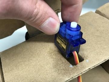 Cut another rectangular hole in front flap of the box. Insert second servo motor into this hole. The fit should be fairly tight so it doesn't fall out accidentally.