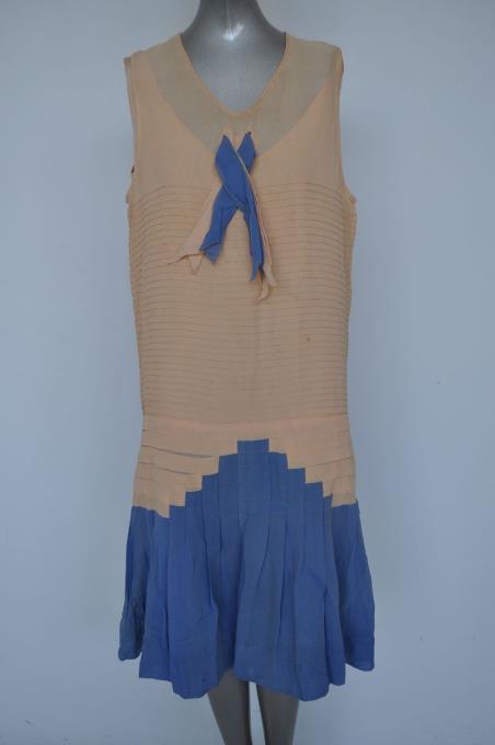 ~Kathy Seldon: Blue evening gown, period style blue pleated shirt, white blouse, lighter color (yellow, or cream) sweater vest. Cloche hat.