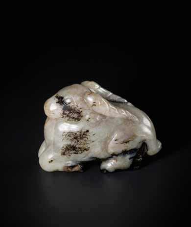 24 A MING DYNASTY MOTTLED JADE CARVING OF A RAM WITH LINGZHI Celadon, brown and black mottled jade, smooth surface polish China, Ming Dynasty This auspicious jade figurine of a recumbent ram shows