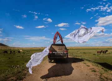 On the roof of a 4WD, long white flags are mounted fluttering in the wind next to an old ger-ring.