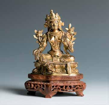 sits dressed in heavy robes that fall in voluminous folds, the Buddha on one side accompanied with a pair of bodhisattvas wearing