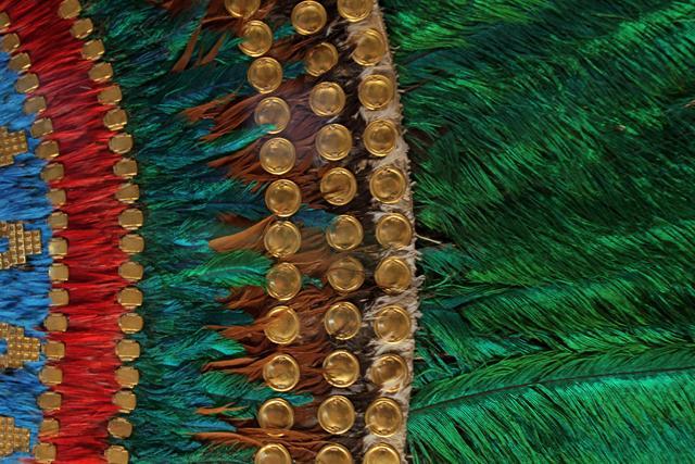 Form The Ruler s Feather Headdress has a base made of valuable materials such as gold, gilded brass, and potentially other metals Protruding vertically from the base are many green and colorful