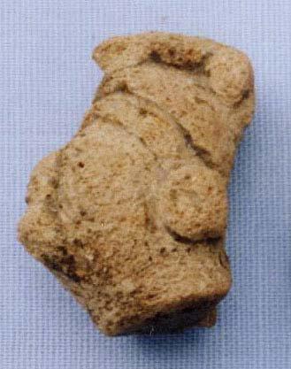 Figurine H-24 is solid with a medium-fine sand temper and incomplete firing. It wears a headdress with a crest over the top. It appears to have facial hair above the lips and on the chin.