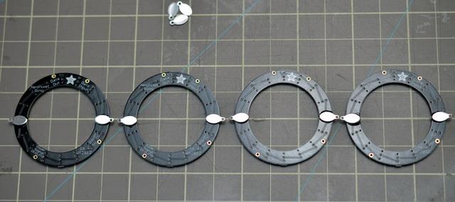 Build it! Lay out four NeoPixel rings on a gridded surface like a cutting mat. Glue on your metal jewelry findings as shown with E6000 craft adhesive and let dry overnight.