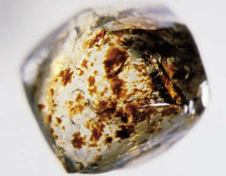 3-34: Dark brown surface spots on an alluvial diamond from Arenapolis, Mato Grosso, Brazil (0.28 ct). The surface also exhibits multiple crescentshaped percussion marks.