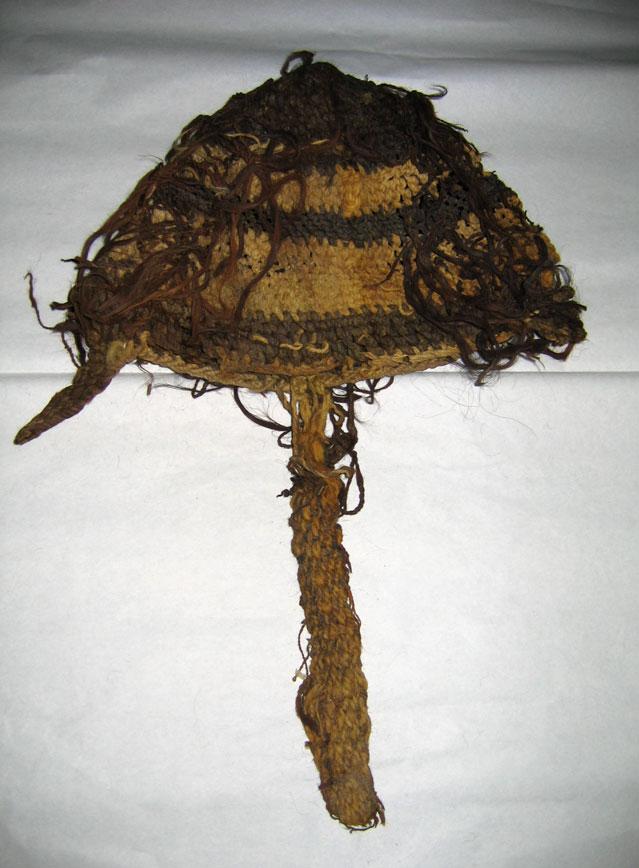 This hat is a woven tube folded almost in half. It is a natural colored grass. The texture is varied with at least nine horizontal bands that are woven in slightly different patterns.