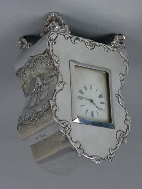 Lot 131 Lot 129 Lot 129 A LATE VICTORIAN/EDWARDIAN SILVER BOUDOIR CLOCK, the front with foliate scroll outline, the sides with embossed Reynolds Angels, white enamel