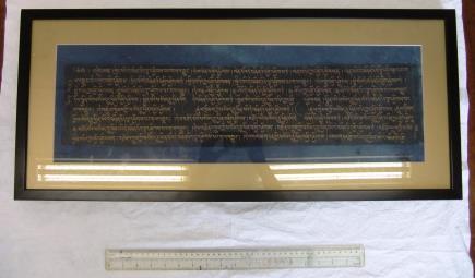 The gold text is visible on both sides and is on black coloured background with a dark blue border. It is in modern glass frame, with a crack on one side.
