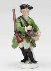 23. A Meissen miniature figure of a sportsman, standing, wearing a green hunting coat and gilt trimmed black tricon hat, a gun over
