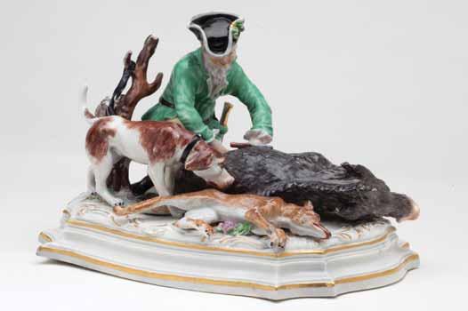 37. A Thuringian porcelain group of a sportsman, kneeling to disembowel a boar, a hound and a dead fox at his side,