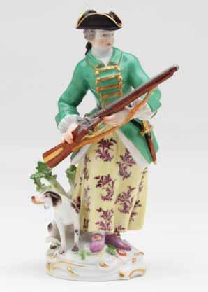 52. A Meissen figure of a sportswoman, standing, wearing a flower patterned skirt, green hunting coat and gilt bordered black tricorn hat, holding a