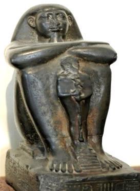 There is a figure for an ancient Egypt deity between his legs. He is wearing a Khat headdress. Fig.25 Block Statue Of Pa-Ankh-Ra [38]. Fig.23 Block Statue of Djedbastefiufankh [36].