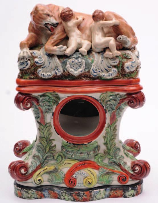 586. A Staffordshire pearl glazed watch group of waisted form with moulded foliate decoration, the corners terminating in scrolls and surmounted by Romulus and Remus at the breast of the wolf on a