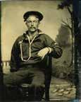 *148. TINTYPE OF A NAVAL SAILOR. 1/6th plate measuring 2 5/8 x 3 1/4. Depicts a studio shot of a seated sailor in full uniform with cap and wearing his bosun whistle lanyard around his neck.