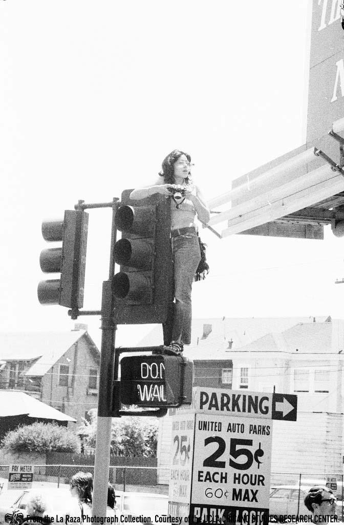 Maria Marquez Sanchez taking photos on top of a traffic light post at an anti-vietnam War