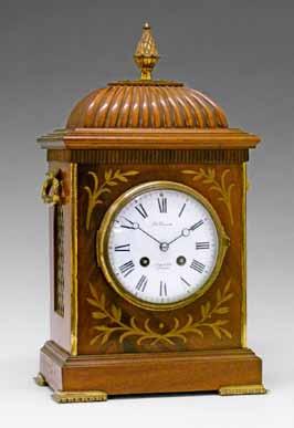 108 Early 20th Century Regency style brass inlaid mahogany mantel clock having a pineapple finial, carrying handles and grilles to the sides and standing on bracket feet, the white enamel dial
