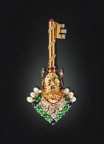 MORONI - A multi-gem set brooch modelled as a crowned mask surmounting a key, set throughout with round brilliant and baguette cut diamonds, emerald cabochons, oval cut sapphires and small round cut